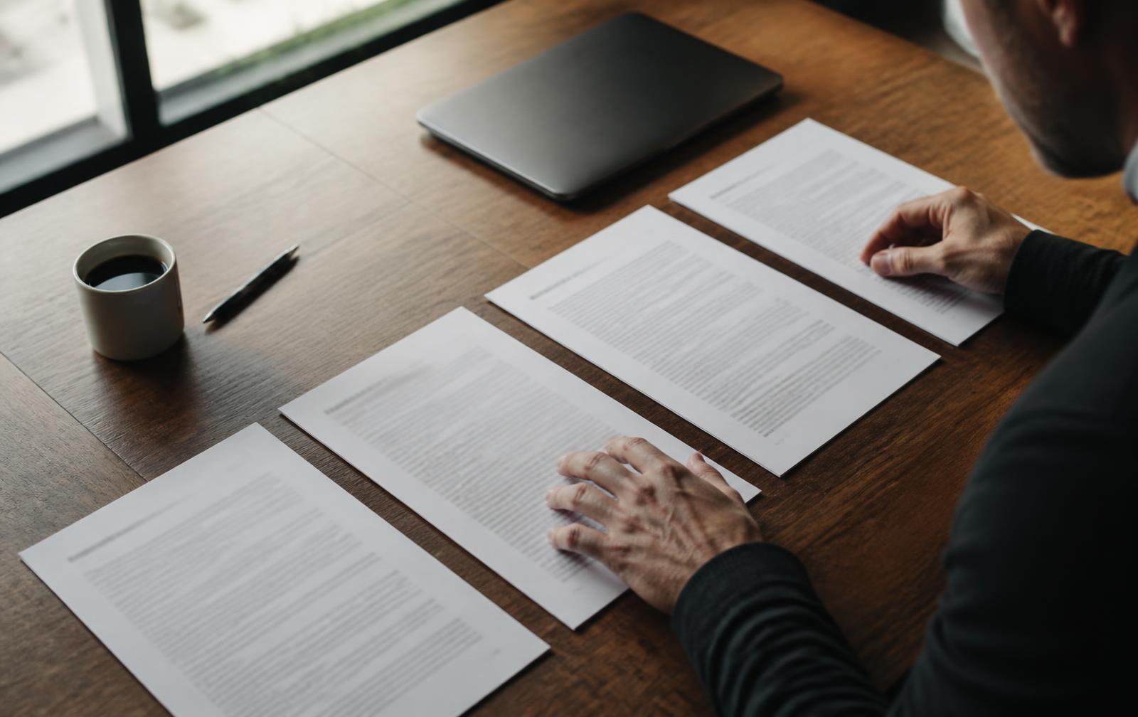 Des mains comparent plusieurs documents imprimés posés côte à côte sur une table en bois.